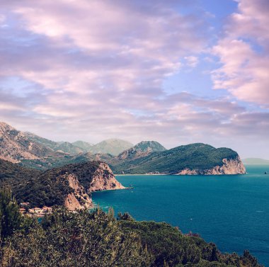 Denizden güneşli bir günde kayaların üzerinde resim gibi bir manzara. Budva Riviera, Karadağ. Karadağ 'ın Budva adası Sveti Nikola' nın hava manzarası. Hawaii plajı, şemsiyeler, banyolar ve kristal berrak sular