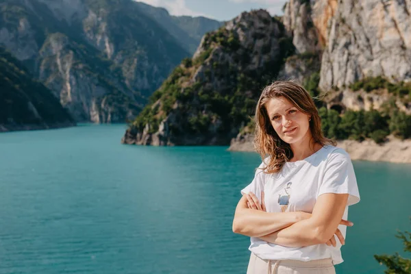 Meisjestoerist staat aan de oever van een meer in de bergen. prachtig landschap, Piva Lake in Montenegro.. Vrouw staat aan de kust van Piva meer bij zonsondergang in de zomer. Landschap met meisje, beroemd — Stockfoto