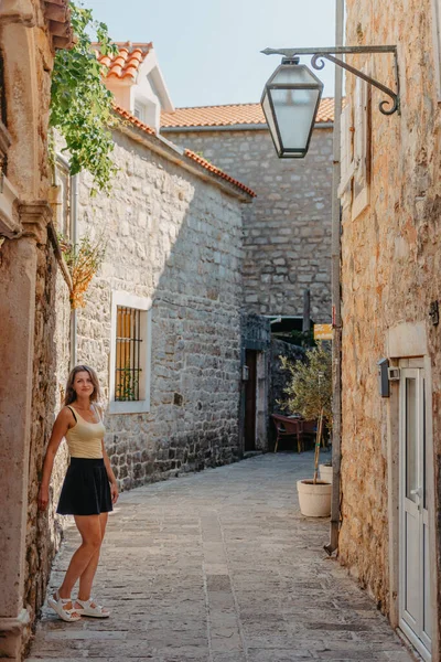 Chica turística caminando por la antigua calle estrecha en un hermoso día de verano en MEDITERRÁNEO MEDIEVAL CITY, BUDVA ANTIGUA, MONTENEGRO. Joven hermosa alegre mujer caminando en la vieja calle en —  Fotos de Stock