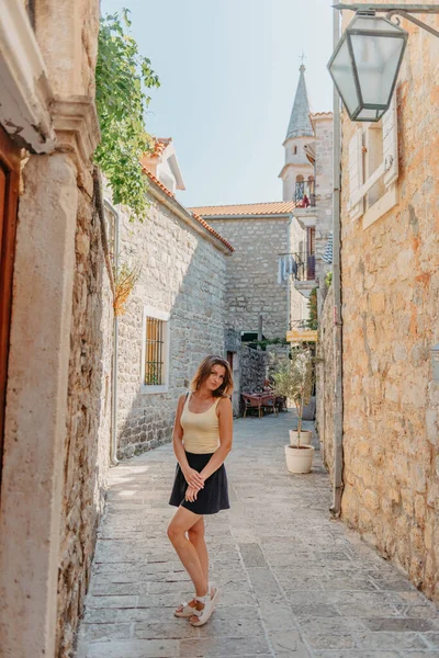 Chica turística caminando por la antigua calle estrecha en un hermoso día de verano en MEDITERRÁNEO MEDIEVAL CITY, BUDVA ANTIGUA, MONTENEGRO. Joven hermosa alegre mujer caminando en la vieja calle en —  Fotos de Stock