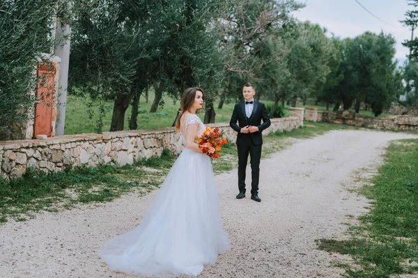 Счастливая стильная улыбающаяся пара, гуляющая в Тоскане, Италия, в день своей свадьбы. Жених и невеста идут по улице руками. Стильная молодая пара гуляет. Муж и жена хорошо общаются. — стоковое фото