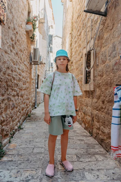 Chica turística caminando por la antigua calle estrecha en un hermoso día de verano en MEDITERRÁNEO MEDIEVAL CITY, BUDVA ANTIGUA, MONTENEGRO. Joven hermosa alegre mujer caminando en la vieja calle en — Foto de Stock