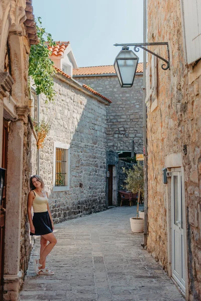 Chica turística caminando por la antigua calle estrecha en un hermoso día de verano en MEDITERRÁNEO MEDIEVAL CITY, BUDVA ANTIGUA, MONTENEGRO. Joven hermosa alegre mujer caminando en la vieja calle en —  Fotos de Stock