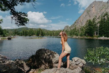 Turist kız gölün, kozalaklı ormanın ve dağlardaki turkuaz gölün kıyısındaki büyük taşın üzerindeki sihirli manzaranın tadını çıkarıyor. Doğal Park 'ta yürüyüş. Tatlı kız.