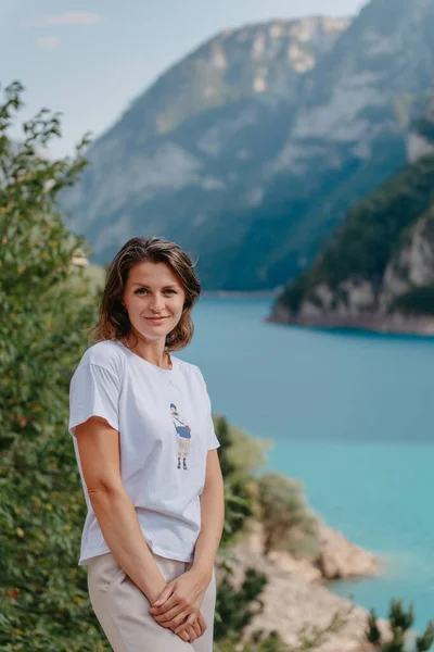 Chica turística se encuentra en la orilla de un lago en las montañas. hermoso paisaje, Lago Piva en Montenegro.. Mujer está de pie en la costa del lago Piva al atardecer en verano. Paisaje con chica, famoso — Foto de Stock