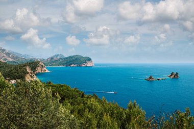 Denizden güneşli bir günde kayaların üzerinde resim gibi bir manzara. Budva Riviera, Karadağ. Karadağ 'ın Budva adası Sveti Nikola' nın hava manzarası. Hawaii plajı, şemsiyeler, banyolar ve kristal berrak sular