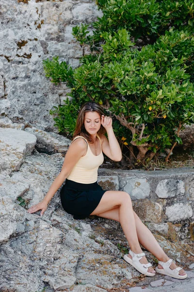 Krásná dívka sedí na kamenné zdi starého města Budva. Dívka sedí na kamenném parapetu, Budva, Černá Hora — Stock fotografie