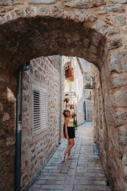 MEDITERRANEAN MEDİEVAL ŞEHRİ, OLD TOWN BUDVA, MONTENEGRO 'DA Güzel bir Yaz Günü' nde Antik Narrow Caddesi 'nde Yürüyen Kız Turist. Genç, güzel, neşeli bir kadın Old Street 'te yürüyor.
