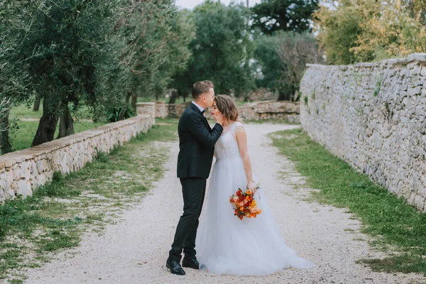 Felice elegante coppia sorridente passeggiando in Toscana, Italia il giorno del loro matrimonio. Gli sposi camminano per strada per le mani. Una giovane coppia elegante cammina. Marito e moglie comunicano bene — Foto Stock