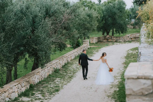 Felice elegante coppia sorridente passeggiando in Toscana, Italia il giorno del loro matrimonio. Gli sposi camminano per strada per le mani. Una giovane coppia elegante cammina. Marito e moglie comunicano bene — Foto Stock