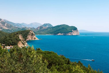 Denizden güneşli bir günde kayaların üzerinde resim gibi bir manzara. Budva Riviera, Karadağ. Karadağ 'ın Budva adası Sveti Nikola' nın hava manzarası. Hawaii plajı, şemsiyeler, banyolar ve kristal berrak sular
