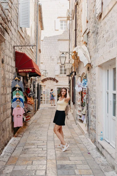 Chica turística caminando por la antigua calle estrecha en un hermoso día de verano en MEDITERRÁNEO MEDIEVAL CITY, BUDVA ANTIGUA, MONTENEGRO. Joven hermosa alegre mujer caminando en la vieja calle en —  Fotos de Stock