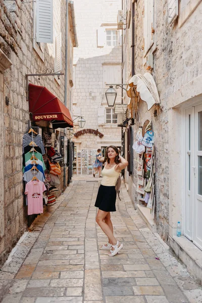 Chica turística caminando por la antigua calle estrecha en un hermoso día de verano en MEDITERRÁNEO MEDIEVAL CITY, BUDVA ANTIGUA, MONTENEGRO. Joven hermosa alegre mujer caminando en la vieja calle en —  Fotos de Stock