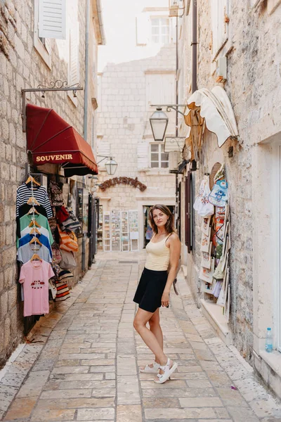 Chica turística caminando por la antigua calle estrecha en un hermoso día de verano en MEDITERRÁNEO MEDIEVAL CITY, BUDVA ANTIGUA, MONTENEGRO. Joven hermosa alegre mujer caminando en la vieja calle en —  Fotos de Stock