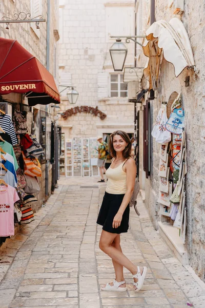 Chica turística caminando por la antigua calle estrecha en un hermoso día de verano en MEDITERRÁNEO MEDIEVAL CITY, BUDVA ANTIGUA, MONTENEGRO. Joven hermosa alegre mujer caminando en la vieja calle en —  Fotos de Stock