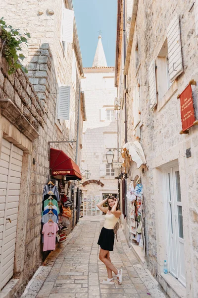 Chica turística caminando por la antigua calle estrecha en un hermoso día de verano en MEDITERRÁNEO MEDIEVAL CITY, BUDVA ANTIGUA, MONTENEGRO. Joven hermosa alegre mujer caminando en la vieja calle en —  Fotos de Stock