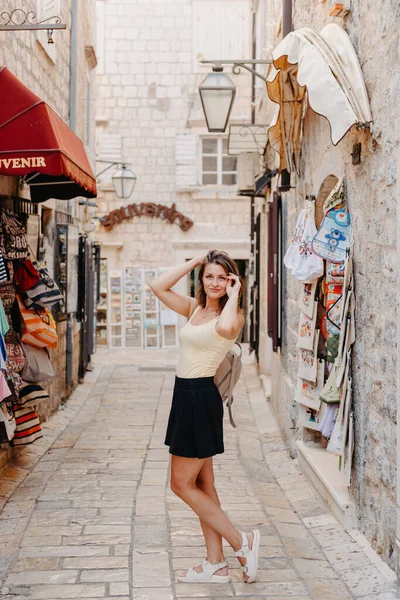 Chica turística caminando por la antigua calle estrecha en un hermoso día de verano en MEDITERRÁNEO MEDIEVAL CITY, BUDVA ANTIGUA, MONTENEGRO. Joven hermosa alegre mujer caminando en la vieja calle en —  Fotos de Stock