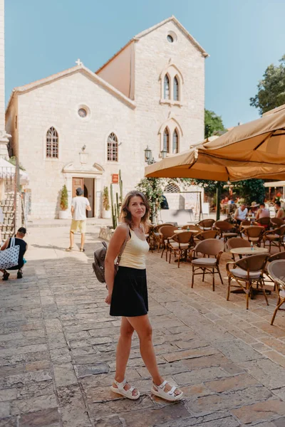 Chica turística caminando por la antigua calle estrecha en un hermoso día de verano en MEDITERRÁNEO MEDIEVAL CITY, BUDVA ANTIGUA, MONTENEGRO. Joven hermosa alegre mujer caminando en la vieja calle en —  Fotos de Stock