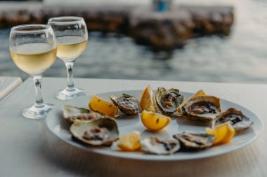 Tabakta taze yakalanmış istiridye ve asma bardakları. Karadağ 'daki istiridye çiftliği yakınlarındaki Kotor Körfezi kıyısında bir restoran. Deniz ürünleri. İstiridye çiftliği ve dağlarıyla güzel bir deniz manzarası, Adriyatik
