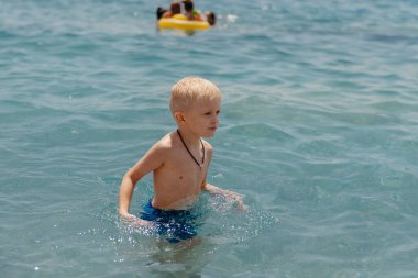 Çocuk tropik tatil köylerinin açık denizinde yüzmeyi öğreniyor. Çocuklar yüzmeyi öğrenir. Küçük çocuklar için egzersiz ve eğitim. Spor kulübünde renkli sörf tahtası olan küçük bir çocuk. Yüzen bebek ya da bebek