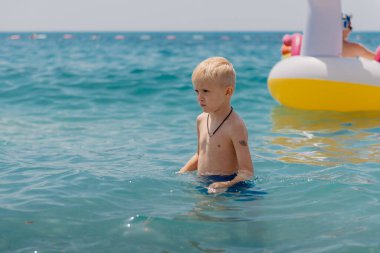 Çocuk tropik tatil köylerinin açık denizinde yüzmeyi öğreniyor. Çocuklar yüzmeyi öğrenir. Küçük çocuklar için egzersiz ve eğitim. Spor kulübünde renkli sörf tahtası olan küçük bir çocuk. Yüzen bebek ya da bebek