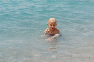 Çocuk tropik tatil köylerinin açık denizinde yüzmeyi öğreniyor. Çocuklar yüzmeyi öğrenir. Küçük çocuklar için egzersiz ve eğitim. Spor kulübünde renkli sörf tahtası olan küçük bir çocuk. Yüzen bebek ya da bebek