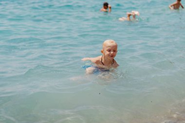 Çocuk tropik tatil köylerinin açık denizinde yüzmeyi öğreniyor. Çocuklar yüzmeyi öğrenir. Küçük çocuklar için egzersiz ve eğitim. Spor kulübünde renkli sörf tahtası olan küçük bir çocuk. Yüzen bebek ya da bebek