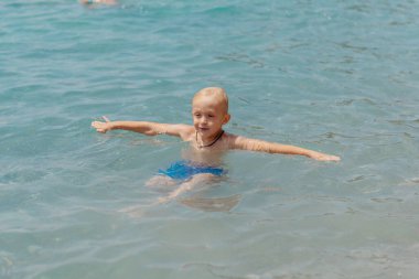 Çocuk tropik tatil köylerinin açık denizinde yüzmeyi öğreniyor. Çocuklar yüzmeyi öğrenir. Küçük çocuklar için egzersiz ve eğitim. Spor kulübünde renkli sörf tahtası olan küçük bir çocuk. Yüzen bebek ya da bebek