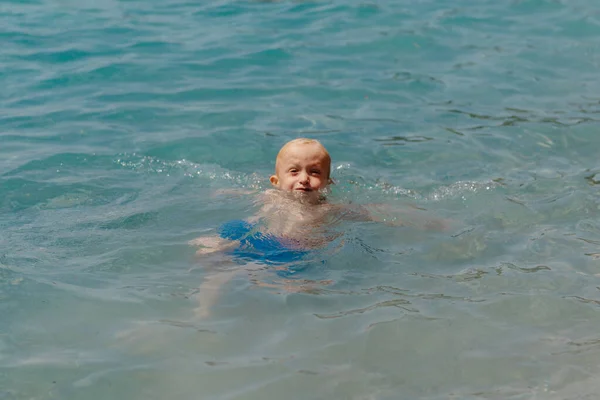 Niño aprendiendo a nadar en el mar abierto del resort tropical. Los niños aprenden a nadar. Ejercicio y entrenamiento para niños pequeños. Niño pequeño con tablero de flotador de colores en el club deportivo. Nadar bebé o niño pequeño — Foto de Stock