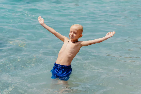 Niño aprendiendo a nadar en el mar abierto del resort tropical. Los niños aprenden a nadar. Ejercicio y entrenamiento para niños pequeños. Niño pequeño con tablero de flotador de colores en el club deportivo. Nadar bebé o niño pequeño — Foto de Stock