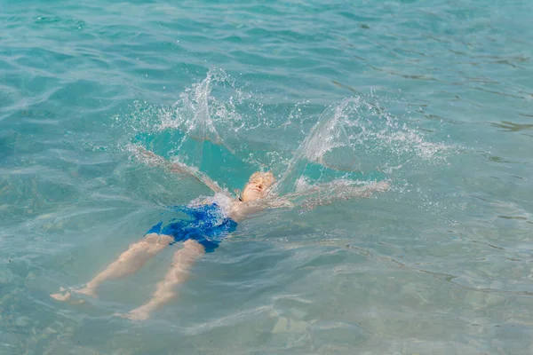 Ребенок учится плавать в открытом море тропического курорта. Дети учатся плавать. Упражнения и тренировки для маленьких детей. Маленький мальчик с красочной доской в спортивном клубе. Плавание ребенка или малыша — стоковое фото