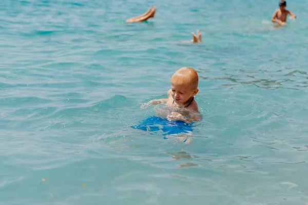 Niño aprendiendo a nadar en el mar abierto del resort tropical. Los niños aprenden a nadar. Ejercicio y entrenamiento para niños pequeños. Niño pequeño con tablero de flotador de colores en el club deportivo. Nadar bebé o niño pequeño — Foto de Stock