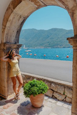 Karadağ 'ın Kotor kentinin sokaklarında yaz fotoğraf çekimi. Beyaz elbiseli ve şapkalı güzel kız. Şapkalı gülümseyen turist kız. Karadağ 'ın fotokopi alanıyla muhteşem manzarası. Moda açık hava fotoğrafı