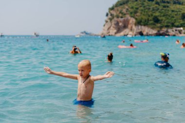 Çocuk tropik tatil köylerinin açık denizinde yüzmeyi öğreniyor. Çocuklar yüzmeyi öğrenir. Küçük çocuklar için egzersiz ve eğitim. Spor kulübünde renkli sörf tahtası olan küçük bir çocuk. Yüzen bebek ya da bebek