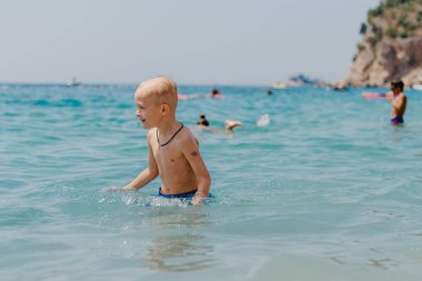 Çocuk tropik tatil köylerinin açık denizinde yüzmeyi öğreniyor. Çocuklar yüzmeyi öğrenir. Küçük çocuklar için egzersiz ve eğitim. Spor kulübünde renkli sörf tahtası olan küçük bir çocuk. Yüzen bebek ya da bebek