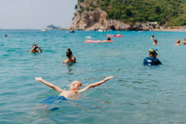 Child learning to swim in the open sea of tropical resort. Kids learn swimming. Exercise and training for young children. Little boy with colorful float board in sport club. Swimming baby or toddler