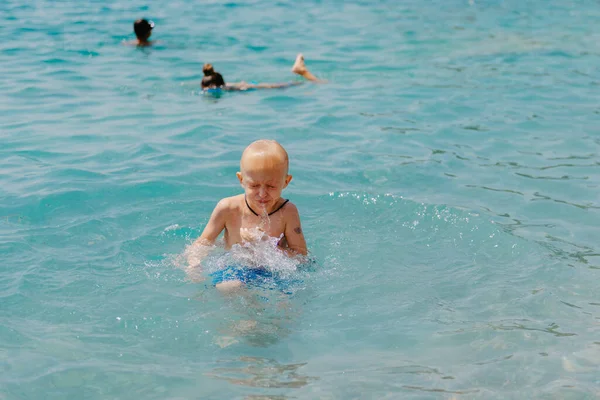Child learning to swim in the open sea of tropical resort. Kids learn swimming. Exercise and training for young children. Little boy with colorful float board in sport club. Swimming baby or toddler