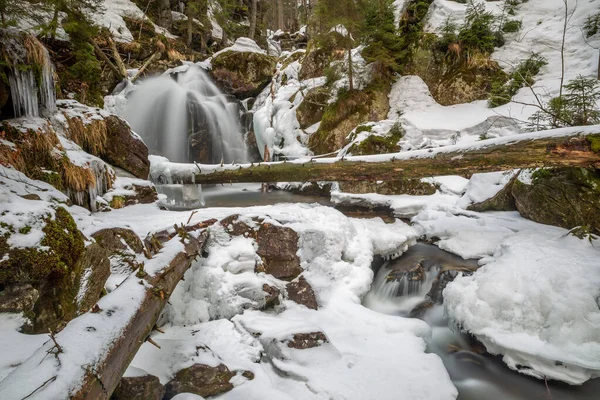river with waterfall and tree trunk in winter long exposure