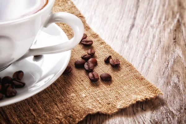 Coffee cup and saucer with coffee beans on a burlap — Stock Photo, Image