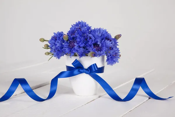 Blauwe korenbloemen in vaas met blauw lint Stockfoto