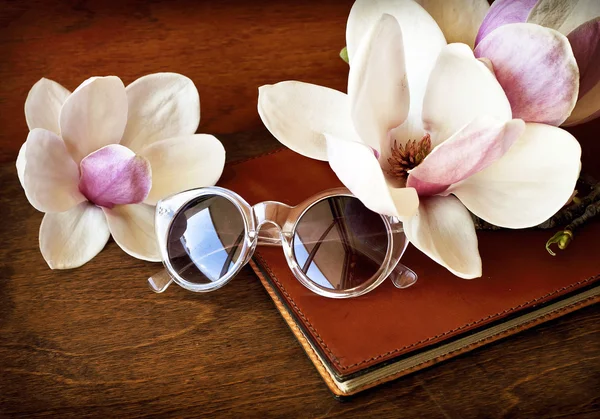 Magnolia blommor med solglasögon och bok — Stockfoto