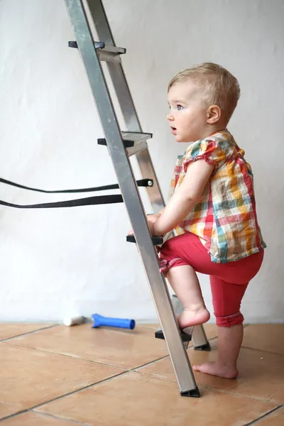 Cute baby girl climbing on a step ladder in domestic room during repair works — Stock Photo, Image