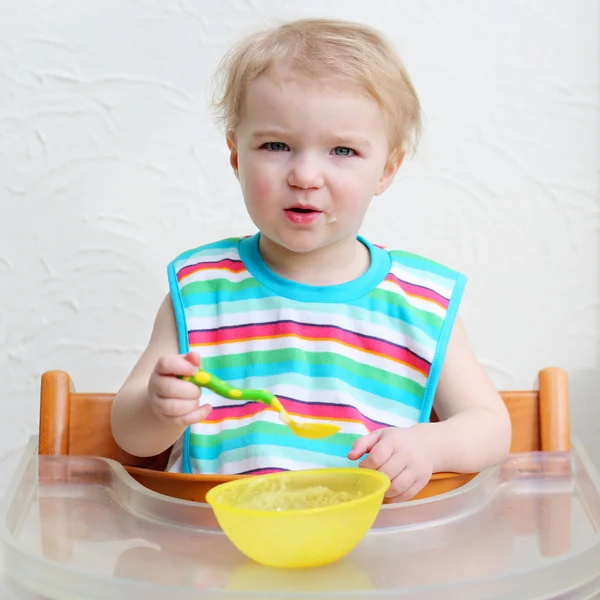 Girl wearing colorful bib eating porridge — Stock Photo, Image