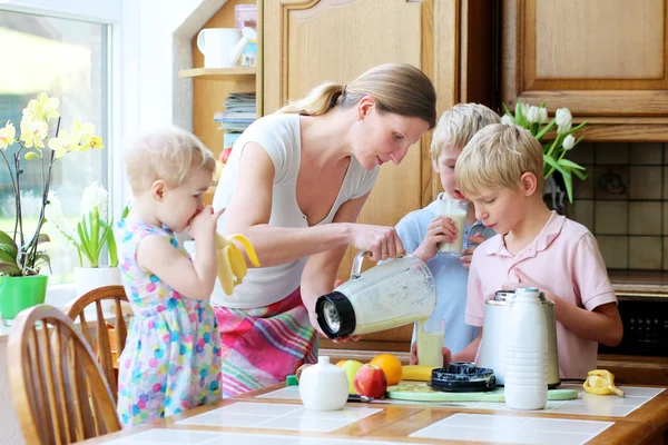 Mamma med tre barn förbereder drink med mjölk och frukt — Stockfoto