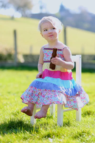 Girl eating tasty chocolate bunny sitting outdoors — Stock Photo, Image