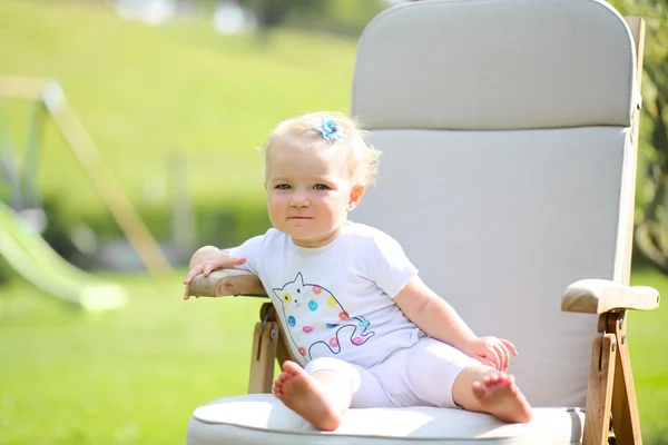 Meisje van de baby ontspannen op een houten teak stoel in een tuin — Stockfoto