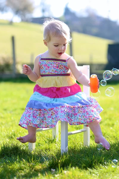 Girl playing with soap bubbles sitting on chair — Stock Photo, Image