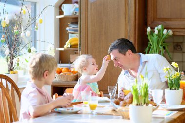 genç oğlu ve yürümeye başlayan çocuk kızı yemek yumurtalı Paskalya günü birlikte güneşli mutfağında oturan aile kahvaltı sırasında baba. seçici odak kız ve erkek.