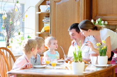 Beş aile: Baba, anne ve 3 çocuğu, genç oğulları ve yürümeye başlayan çocuk kızı yumurta Paskalya günü birlikte güneşli mutfağında oturan aile kahvaltı sırasında yeme. seçici odak üstünde küçük kız.