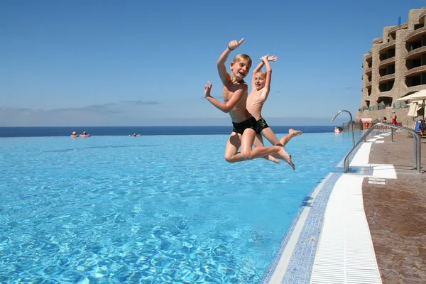 Dos hermanos gemelos felices están saltando a la piscina infinita en el complejo con el océano al fondo —  Fotos de Stock